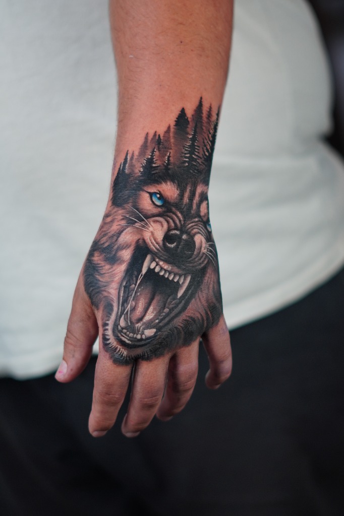 Growling wild wolf with intense blue eyes and pine trees tattooed on the hand