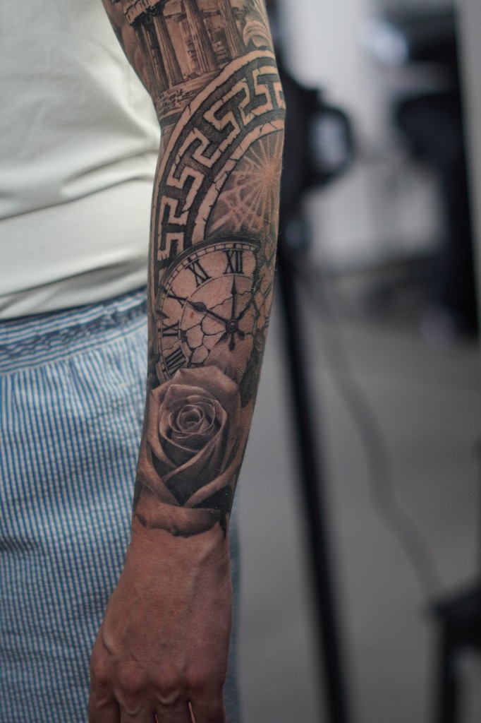 Roman numeral clock, realistic rose and Greek meander frieze tattooed on a forearm